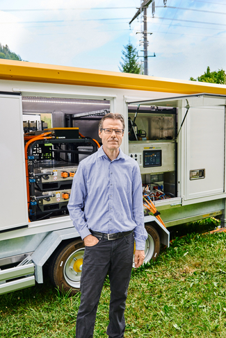 Adrian Bachmann, Leiter Gebiet Mittelland Ost bei BKW Power Grid, vor einer hybriden Netzersatzanlage, ein mobiler Notstromgenerator mit Batterie.