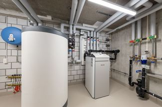 Local technique avec un grand chauffe-eau à accumulation, une installation de chauffage moderne, des con-duites bien posées ainsi que différents éléments d’armatures et de régulation sur le mur.