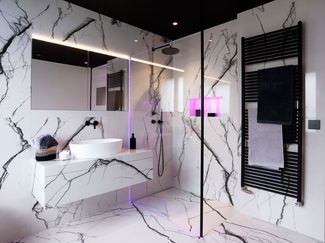 Modernes Badezimmer mit grossformatigen Marmorfliesen, begehbarer Dusche mit Regenbrause, beleuchtetem Wandnischenfach, wandhängendem Waschtisch und schwarzem Handtuchheizkörper.