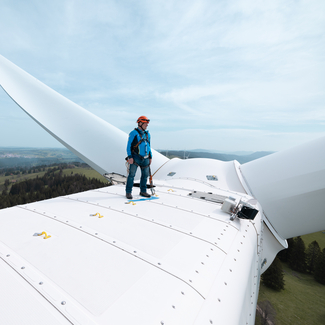 Mann steht zuoberst auf weisser Windturbine und schaut in die Ferne