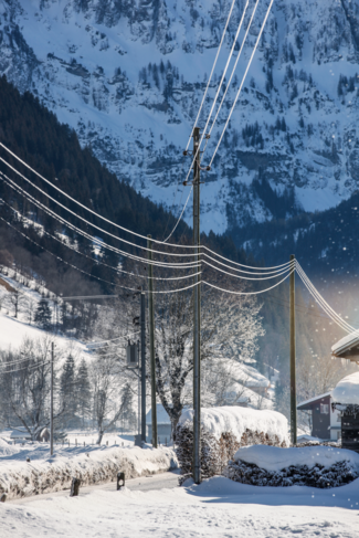 Das Bild zeigt eine Stromleitung der Netzebene 3 im Winter. Im Hintergrund ist eine schneebedeckte Felswand zu sehen.