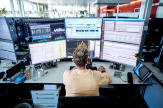 Ein Mann sitzt vor sechs Bildschirme. Er schaut auf die Monitore. Das Foto ist