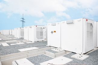 Nell'immagine, è visibile un accumulatore di batterie bianco davanti a un traliccio elettrico.