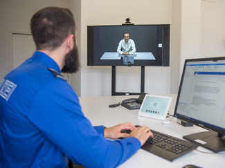 Polizist vor Computer. Auf zweitem Bildschirm läuft eine Videokonferenz