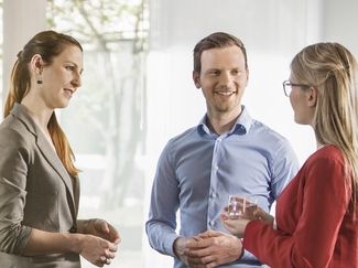 Zwei Frauen und 1 Mann unterhalten sich stehend