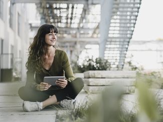 [Translate to Englisch (CH):] Frau mit Tablet bewirbt sich online und sitzt dabei draussen