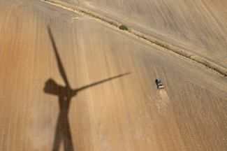Prise de vue d'une éolienne vers le bas sur un champ avec l'ombre d'une éolienne et d'un tracteur.