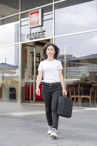 Jeune femme en T-shirt blanc, pantalon noir et mallette sortant d'un café