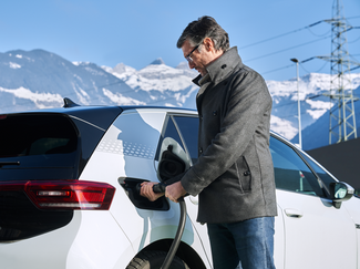 Mann lädt weisses E-Auto vor Bergpanorama